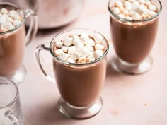 two mugs filled with hot chocolate and marshmallows sitting on a table