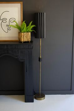 a black and gold floor lamp next to a painting on a fireplace mantel with a potted plant in the corner