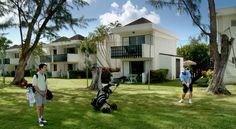 two men are standing in the grass with golf gear and an umbrella near some apartment buildings