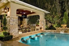 an outdoor kitchen and pool area with stone pillars around the pool, covered in lights