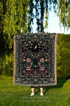 a woman standing in front of a tree holding up a blanket with flowers on it