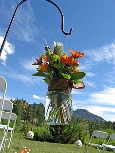 a mason jar filled with flowers sitting on top of a grass covered field next to white chairs