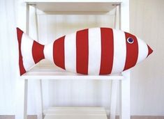 a red and white striped fish pillow sitting on top of a wooden chair next to a shelf