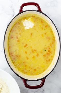 a red pot filled with yellow food next to a white bowl full of flour on a marble counter top