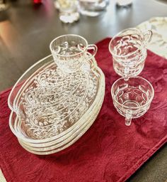 glass dishes and cups are sitting on a red placemat