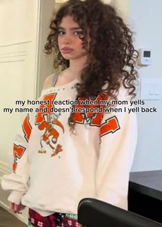 a woman with long curly hair standing in front of a mirror wearing an orange and white sweatshirt