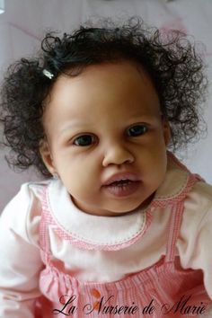 a baby girl with curly hair wearing a pink dress