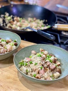 two bowls filled with rice and meat on top of a wooden table next to a skillet