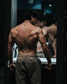 a man standing in front of a mirror with his back turned to the camera and no shirt on