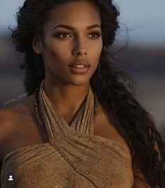 a woman with long black hair wearing a brown dress and posing for a photo in the desert