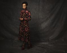 a woman standing in front of a black backdrop wearing a dress with flowers on it