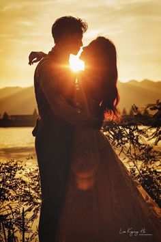 a man and woman are kissing in front of the sun at their wedding day, with mountains in the background