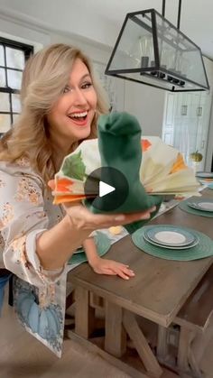 a woman holding up a green hat in front of a table with plates and napkins