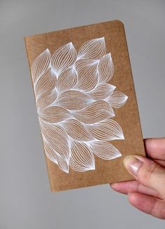 a hand holding a piece of brown paper with white designs on it and a card in the other hand