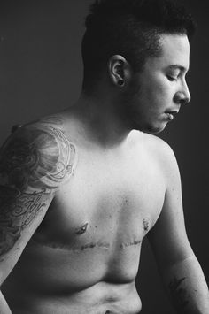 black and white photograph of a man with tattoos on his chest looking down at something