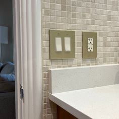 a bathroom sink with two switches on the wall and a couch in the back ground