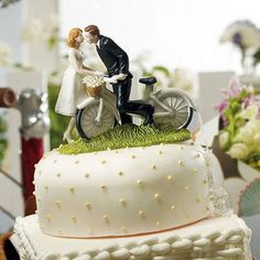 a wedding cake with a bride and groom on the bike topper, surrounded by flowers