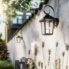 a light hanging on the side of a building next to flowers and plants in front of it