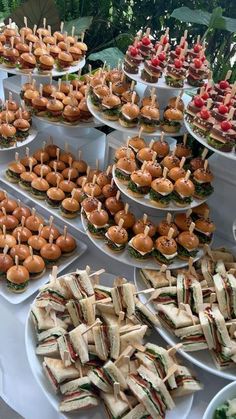 many sandwiches are arranged on trays with toothpicks stuck in them to eat