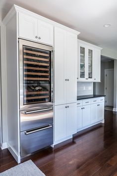 a kitchen with white cabinets and stainless steel appliances in the center, along with hardwood flooring