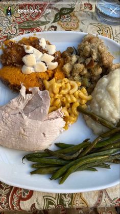 a white plate topped with meat, macaroni and cheese next to green beans