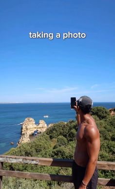 a man taking a photo with his cell phone near the ocean and cliffs that surround him