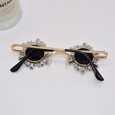 Add a burst of sparkle to your look with these show-stopping, round sunglasses. Featuring a wire-frame design adorned with extended rhinestones, these shades deliver a surrealistic, avant-garde aesthetic. Perfect for standing out at festivals, high-fashion events, or anywhere you want to make a statement. The gold-tone frame adds a touch of luxury, while the oversized rhinestone embellishments ensure you’ll shine from every angle. Black Metal Sunglasses For Party, Black Metal Sunglasses For Parties, Black Metal Party Sunglasses, Gold Anti-reflective Sunglasses For Parties, Gold Metal Sunglasses For Party, Party Sunglasses With Anti-reflective Glass, Gold Party Sunglasses With Adjustable Fit, Modern Metal Sunglasses For Parties, Adjustable Metal Sunglasses For Party