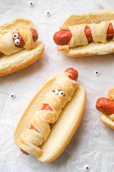 four hotdogs with googly eyes and wrapped in bread on top of white paper