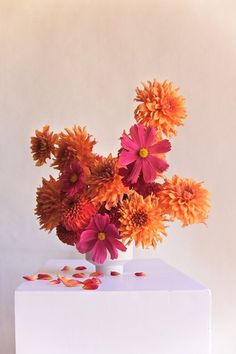 an arrangement of flowers in a white vase on a table with confetti scattered around it