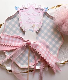 a pink and white cake topper sitting on top of a piece of paper with ribbon around it