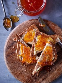 two pieces of toast with an egg in the middle on a cutting board next to honey and spoons