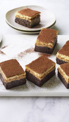 four pieces of cake sitting on top of a white plate next to two plates with desserts