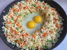 two eggs on top of rice in a skillet with carrots and green onions