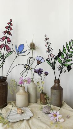 several vases with flowers and plants in them on a cloth covered tablecloth next to a white wall