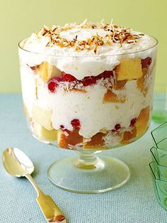 a trifle with fruit and nuts in a glass dish next to a spoon on a table