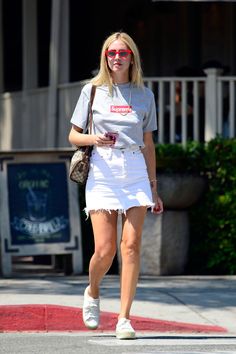 a woman walking down the street wearing a white skirt and t - shirt with red lettering on it