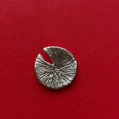 a silver brooch sitting on top of a red leather surface with a circle shaped object in the middle