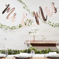 the table is set with white plates and place settings for an elegant wedding reception in front of a brick wall decorated with greenery