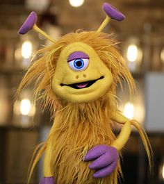 a close up of a stuffed animal with very long hair and blue eyes, standing in front of some lights