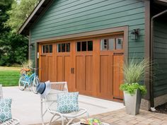 two white chairs sitting in front of a green building with a brown garage door and windows