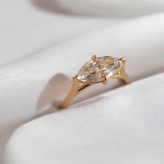 a gold ring with two pear shaped diamonds on white satin material, close up view