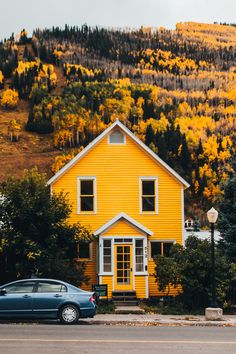 a blue car parked in front of a yellow house on the side of a road