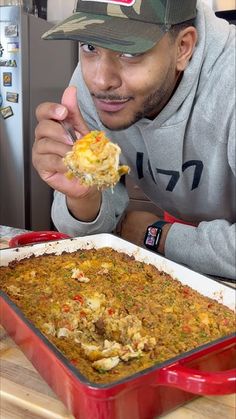 a man in a baseball cap eating food from a casserole dish