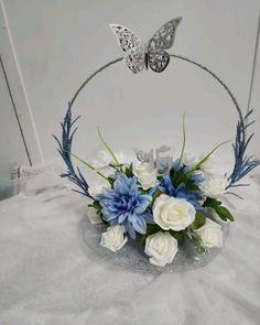 a white and blue flower arrangement in a glass bowl with butterfly decoration on the top