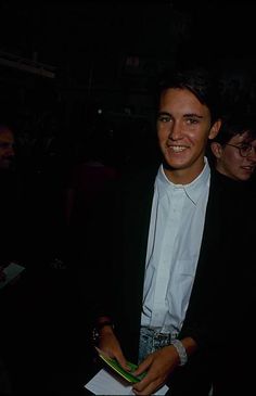 a man in a black suit and white shirt smiling at the camera while holding a book