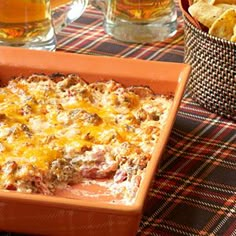 a casserole dish on a table with chips and beer