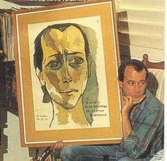 a man sitting in front of a painting holding up a large framed art piece with a woman's face on it