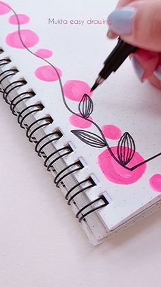 a person is writing on a spiral notebook with pink circles and black lines around it