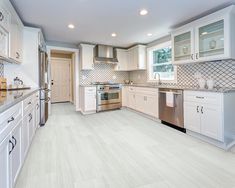 an empty kitchen with white cabinets and silver appliances in the center, along with marble counter tops