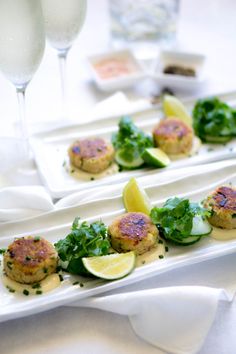 two white plates topped with crab cakes and cucumbers next to a glass of wine